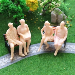 May include: Four miniature plastic figures of people sitting on a park bench. The figures are all wearing casual clothing and are painted in a light skin tone.