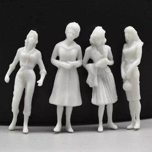 Puede incluir: Conjunto de cuatro figuras en miniatura de plástico blanco que representan personas. Las figuras están vestidas con diferentes estilos de ropa, incluyendo un abrigo, un vestido y pantalones.