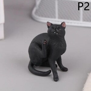 May include: A black cat figurine in a seated position, scratching its ear. The cat has pink inner ears and paw pads. The figurine is on a gray surface, with the text "P2" in the upper right corner.