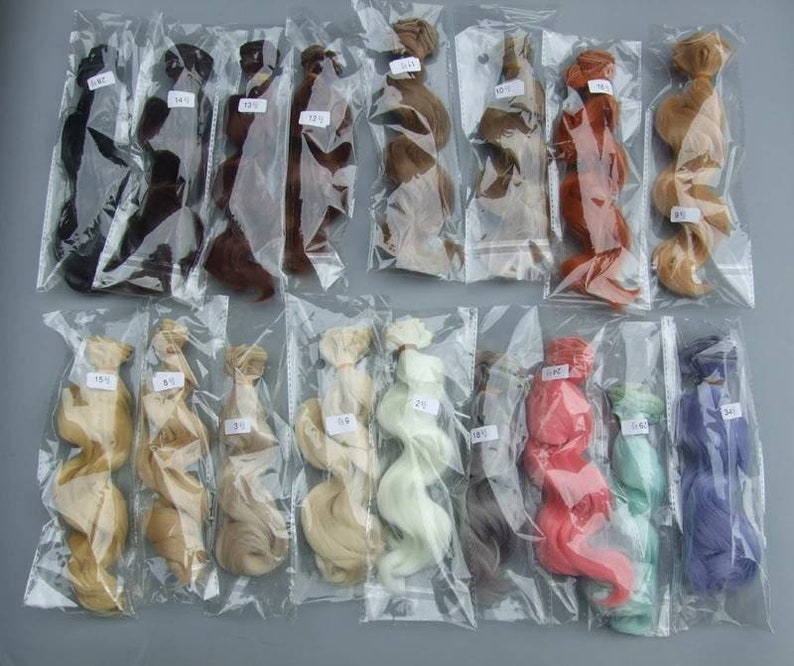 May include: Assortment of 14 different colored doll hair pieces in individual plastic bags. The hair is in various lengths and textures, including straight, wavy, and curly.