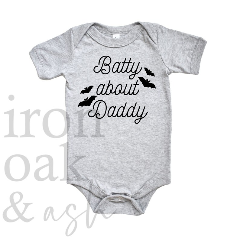 May include: A gray baby onesie with the text "Batty about Daddy" in black cursive font. There are five black bat silhouettes around the text.