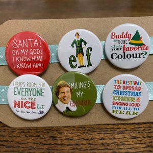 May include: Six round button badges featuring characters and quotes from the film Elf. The badges are red, green, white and yellow with black text. The text on the badges includes "Santa! Oh my god! I know him! I know him!" "Buddy the EIC what's your favourite Colour?" "There's room for everyone on the nice list" "Smiling's my favourite" and "The best way to spread Christmas cheer singing loud for all to hear."
