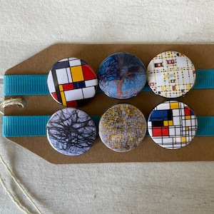 May include: Six round, colorful, printed buttons with different abstract designs. The buttons are arranged in two rows of three on a brown card with blue ribbon.