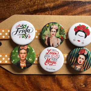 May include: Set of six round button badges featuring Frida Kahlo. The badges feature different images of Frida Kahlo, including a portrait, a quote, and a floral design. The badges are white with colourful designs.