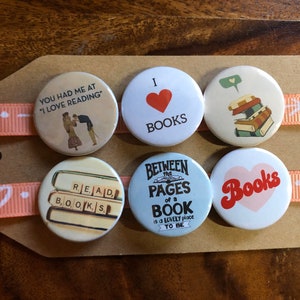 Puede incluir: Seis botones redondos con diseños de temática de libros. Los botones presentan un corazón rojo con el texto "Me encantan los libros", una pila de libros con un globo de diálogo, una máquina de escribir con el texto "Leer libros", un corazón con el texto "Libros", una pila de libros con el texto "Entre las páginas de un libro es un lugar encantador para estar", y una pareja con el texto "Me conquistaste con "Me encanta leer"".