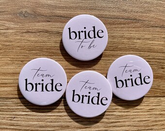 May include: Four round pink buttons with white text. One button says "bride to be". Three buttons say "team bride".