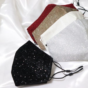 Puede incluir: Cuatro mascarillas faciales brillantes en rojo, dorado, blanco y negro. Las mascarillas están hechas de una tela suave y brillante y tienen lazos para las orejas ajustables.