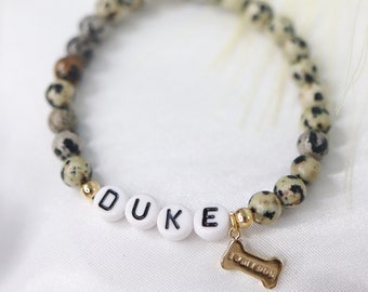 May include: A speckled brown and white beaded bracelet with a gold charm that says "I love my dog" and white letter beads spelling out the name "DUKE".
