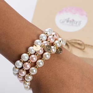 May include: Three layered bracelets with white and pink pearls and gold accents. Each bracelet has a small gold charm with a letter on it.