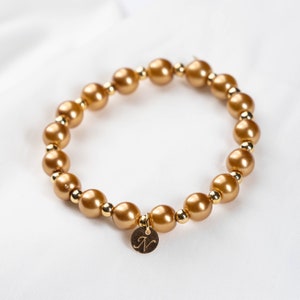 May include: A gold beaded bracelet with a gold charm that has the letter "N" engraved on it.