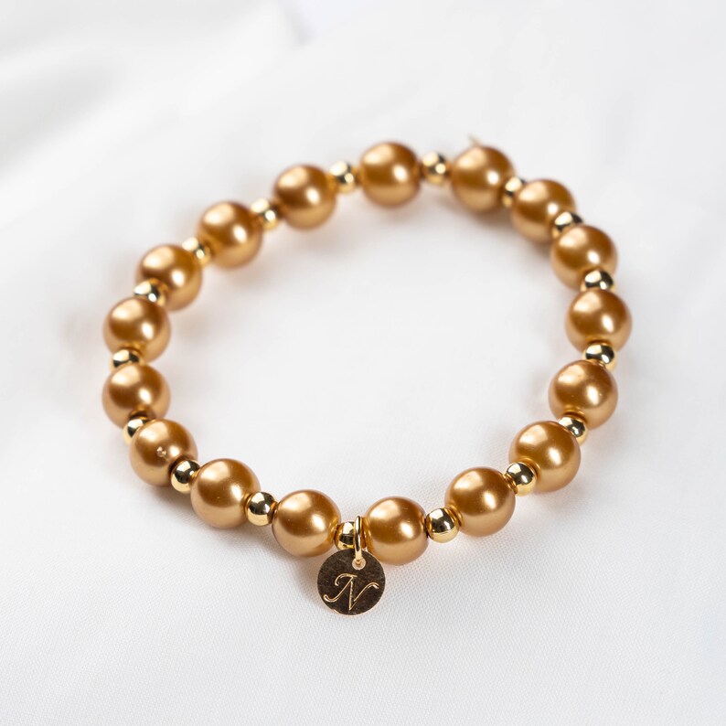 May include: A gold beaded bracelet with a gold charm that has the letter "N" engraved on it.