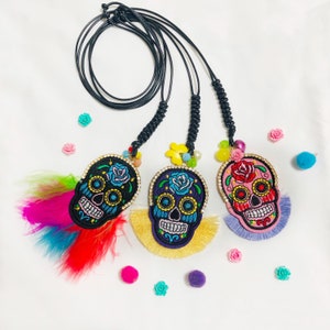 May include: Three colorful embroidered skull necklaces with black cords and tassels. The skulls are decorated with flowers and rhinestones.