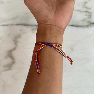 May include: A colorful friendship bracelet with red, yellow, and blue threads tied in a knot. The bracelet is worn on a person's wrist.
