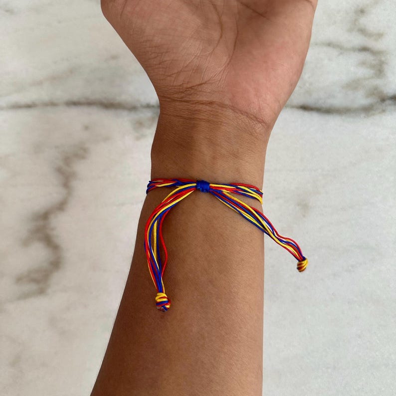 May include: A colorful friendship bracelet with red, yellow, and blue threads tied in a knot. The bracelet is worn on a person's wrist.