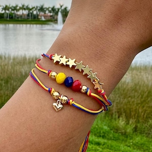 May include: Three layered bracelets with red, yellow, and blue string, gold star charms, and small gold heart charm.