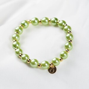 May include: A green pearl bracelet with a gold charm that has the letter "O" on it.