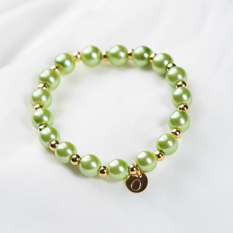 May include: A green pearl bracelet with a gold charm that has the letter "O" on it.