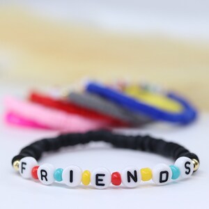 May include: A black elastic bracelet with white beads spelling out the word "FRIENDS". The beads are decorated with red, yellow, and turquoise accents.