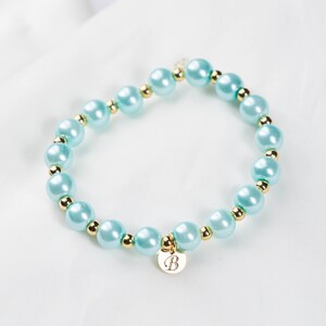May include: A light blue beaded bracelet with gold accents and a gold charm with the letter "B" engraved on it.