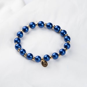 May include: A blue and gold beaded bracelet with a gold charm. The charm has the letter "D" on it.