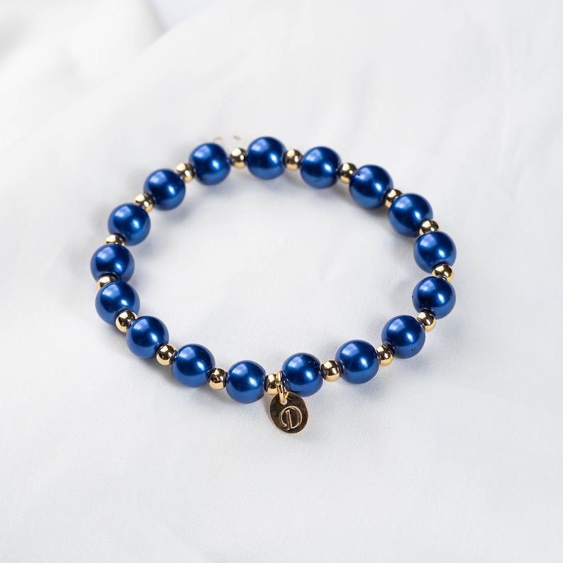 May include: A blue and gold beaded bracelet with a gold charm. The charm has the letter "D" on it.