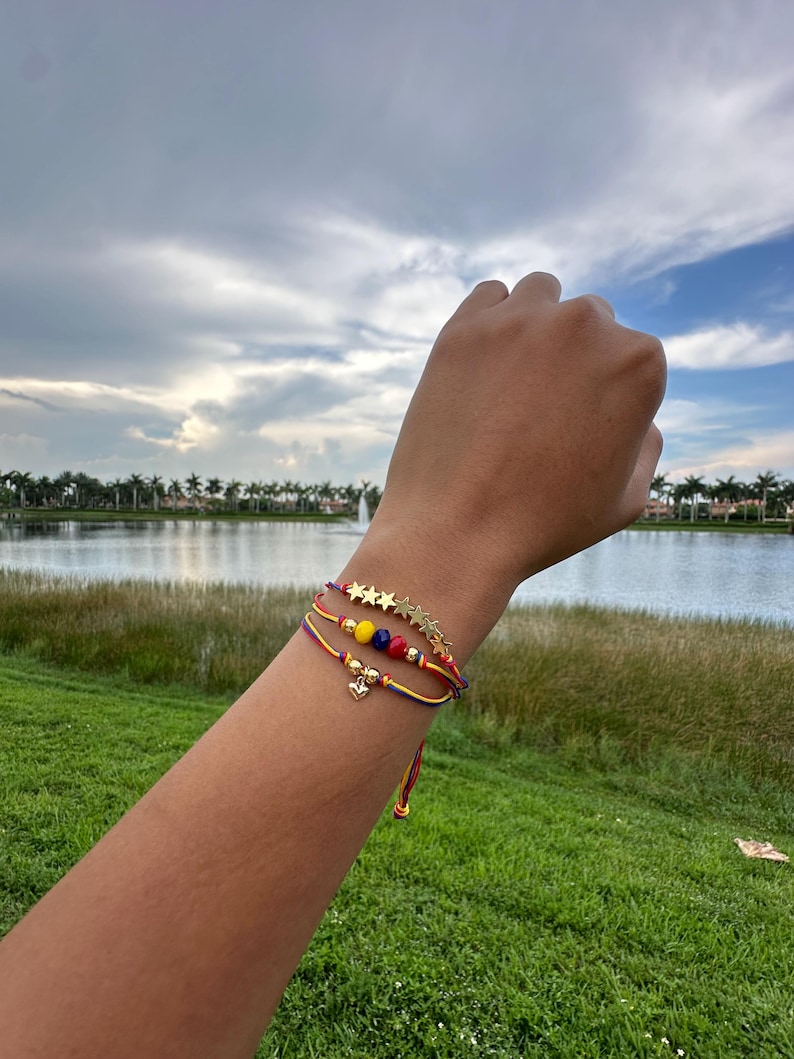 May include: Three colorful string bracelets with gold stars and beads. The bracelets are worn on a person's wrist.