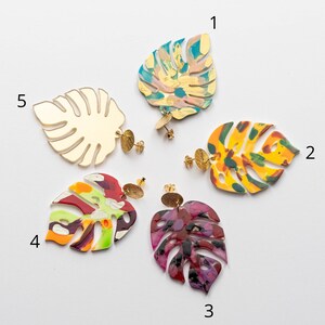 Puede incluir: Cinco pares de pendientes de tono dorado con un dise&ntilde;o de hoja tropical. Cada hoja es de un color y un patr&oacute;n diferente, incluyendo amarillo, rojo, azul y verde.