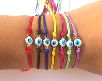 Può includere: Un set di otto braccialetti colorati in corda, ognuno con un ciondolo di occhio blu. I braccialetti sono rosso, nero, blu, giallo, rosa, verde e viola.