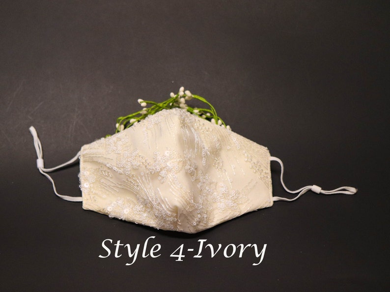 May include: Ivory white face mask with delicate lace and bead embellishments. The mask has adjustable elastic ear loops and is decorated with a sprig of white flowers.