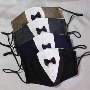 May include: Five face masks with different colored fabrics and bow ties. The masks are layered on top of each other, with the black mask on the bottom and the brown mask on top. The bow ties are all different colors, including black, navy blue, and white.