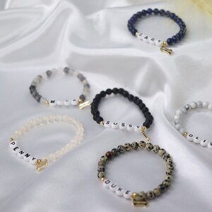 Peut inclure: Plusieurs bracelets de perles avec des lettres blanches &eacute;pelant des noms tels que "Penny", "Duke" et "Gary". Chaque bracelet a un charme dor&eacute;, certains en forme d'os. Les bracelets sont de diff&eacute;rentes couleurs, dont le noir, le blanc et le mouchet&eacute;.