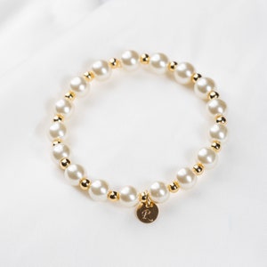 May include: A white pearl bracelet with gold beads and a gold charm with the letter 'R' on it.