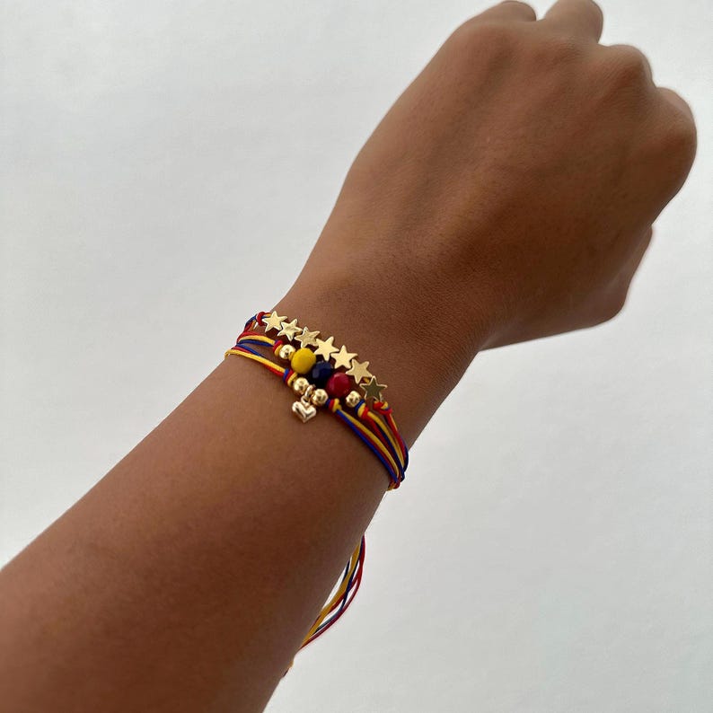 May include: A multi-strand bracelet with red, yellow, and blue string. The bracelet has gold stars and beads, and a small gold heart charm.