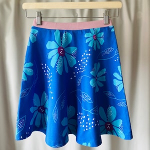 Könnte beinhalten: Ein blauer Rock mit einem rosa Bund und einem Blumendruck. Die Blumen sind blau, grün und lila.