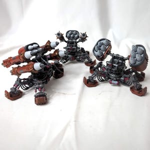 May include: Three miniature robotic combat vehicles with multi-legged bases, metallic copper-coloured armour plating, and dark grey mechanical joints. Each unit features mounted missile launchers with grey projectiles and intricate mechanical details.