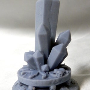 May include: A gray crystal sculpture featuring a large central crystal and several smaller crystals. The crystals are mounted on a circular base with decorative skulls and gear-like shapes. The sculpture is made of a solid, matte material.