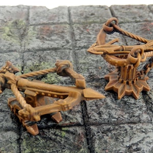 Könnte beinhalten: Zwei Miniatur-Katapulte aus Holz, eines mit einem Seil und das andere mit einer Kette, sind auf einer strukturierten Steinoberfläche zu sehen.