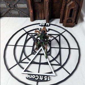 May include: A black plastic template with a white triangle and concentric circles. The template has the text "15 ft cone" and "20 ft" printed on it. A miniature figure is standing on the template.