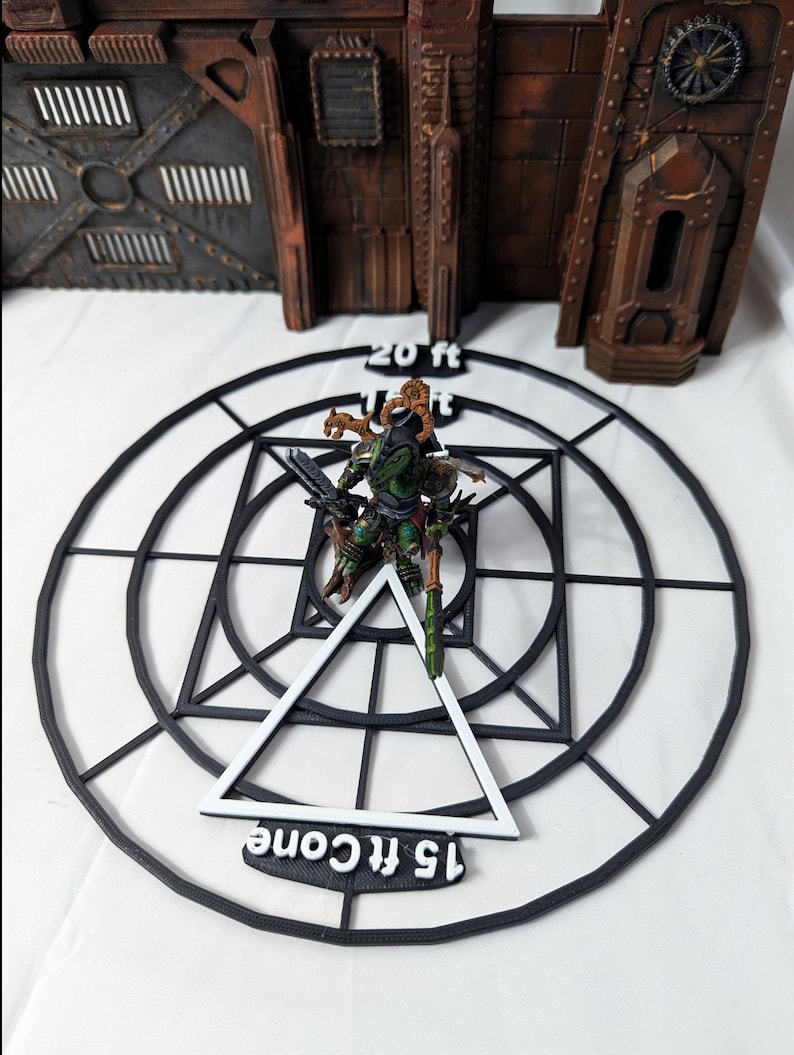 May include: A black plastic template with a white triangle and concentric circles. The template has the text "15 ft cone" and "20 ft" printed on it. A miniature figure is standing on the template.