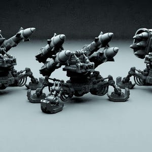 Może przedstawiać: Trzy szare, robotyczne, trójnożne wyrzutnie rakiet z wieloma rurami rakietowymi. Każda wyrzutnia ma inną konfigurację rur rakietowych.