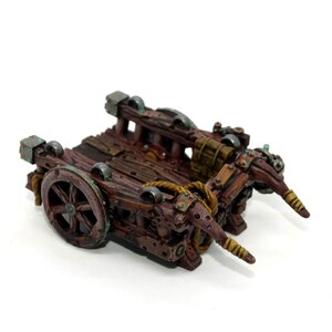 May include: A wooden miniature cart with two wheels, a rope, and two wooden arms. The cart is painted brown with green and gold accents.