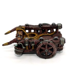 May include: A wooden siege weapon with a rope and a large wheel. The weapon is painted brown and has metal accents.