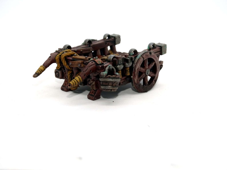 May include: A miniature wooden catapult with a brown and green paint scheme. The catapult has a single wheel and two arms that are raised up.