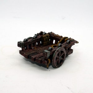 May include: A miniature wooden cart with a single wheel, painted in brown and green tones. The cart has a wooden frame and a rope tied to the back. There is a small brown bag in the cart.