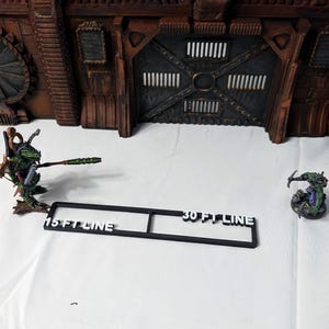 May include: Black plastic ruler with white text that reads "15 FT LINE" and "30 FT LINE". The ruler is on a white surface.