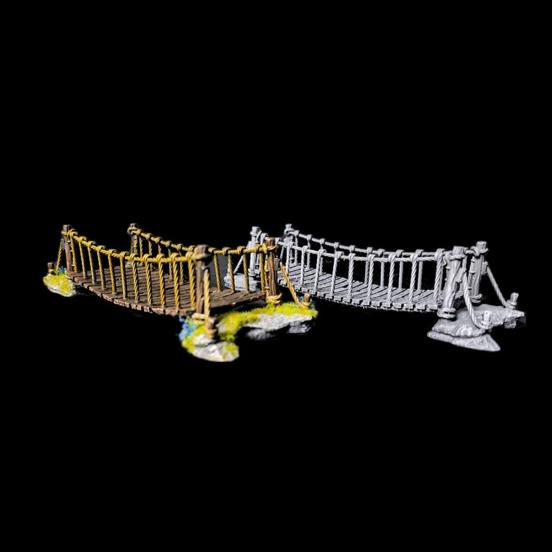 May include: Two miniature rope bridges, one brown and one grey, with wooden supports and rope railings. The bridges are set on a rocky base and are ready for miniature figures to cross.