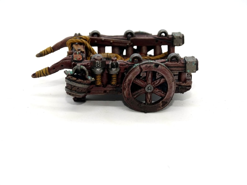 May include: A wooden miniature catapult with a brown and tan paint scheme. The catapult has a rope and a wheel.