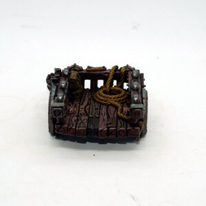 May include: A miniature wooden cart with metal accents and a rope tied to the back. The cart is painted brown with green and silver accents.