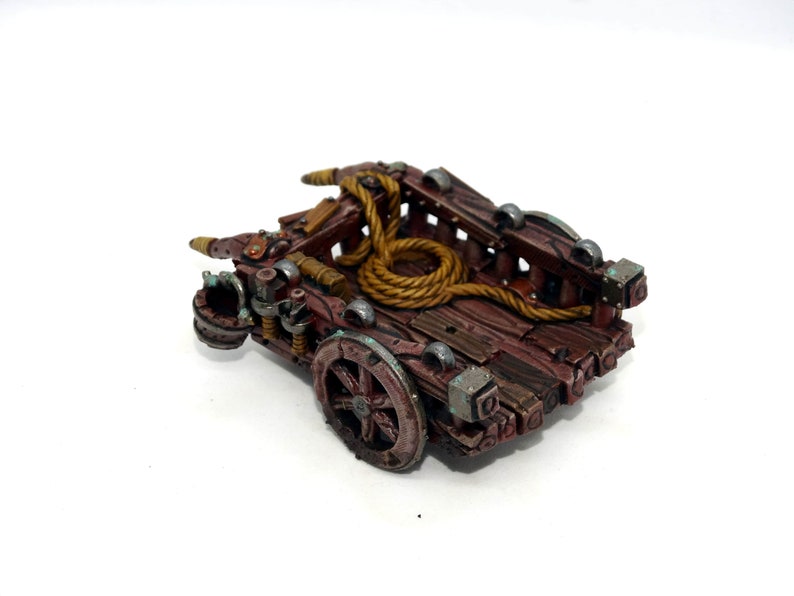 May include: A miniature wooden cart with a rope coiled inside. The cart has a brown wooden base with metal accents and a single wheel. The cart is painted in shades of brown, gold, and silver.
