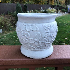 May include: White ceramic planter with a floral design. The planter has a rounded body and a wide rim.